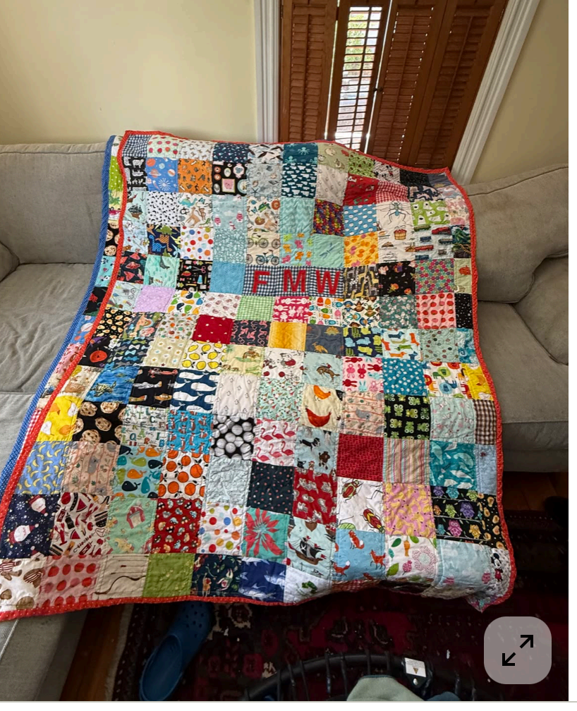 A patchwork memory quilt made from many small printed fabric squares, with the initials FMW appliquéd in red near the center, draped over a sofa.