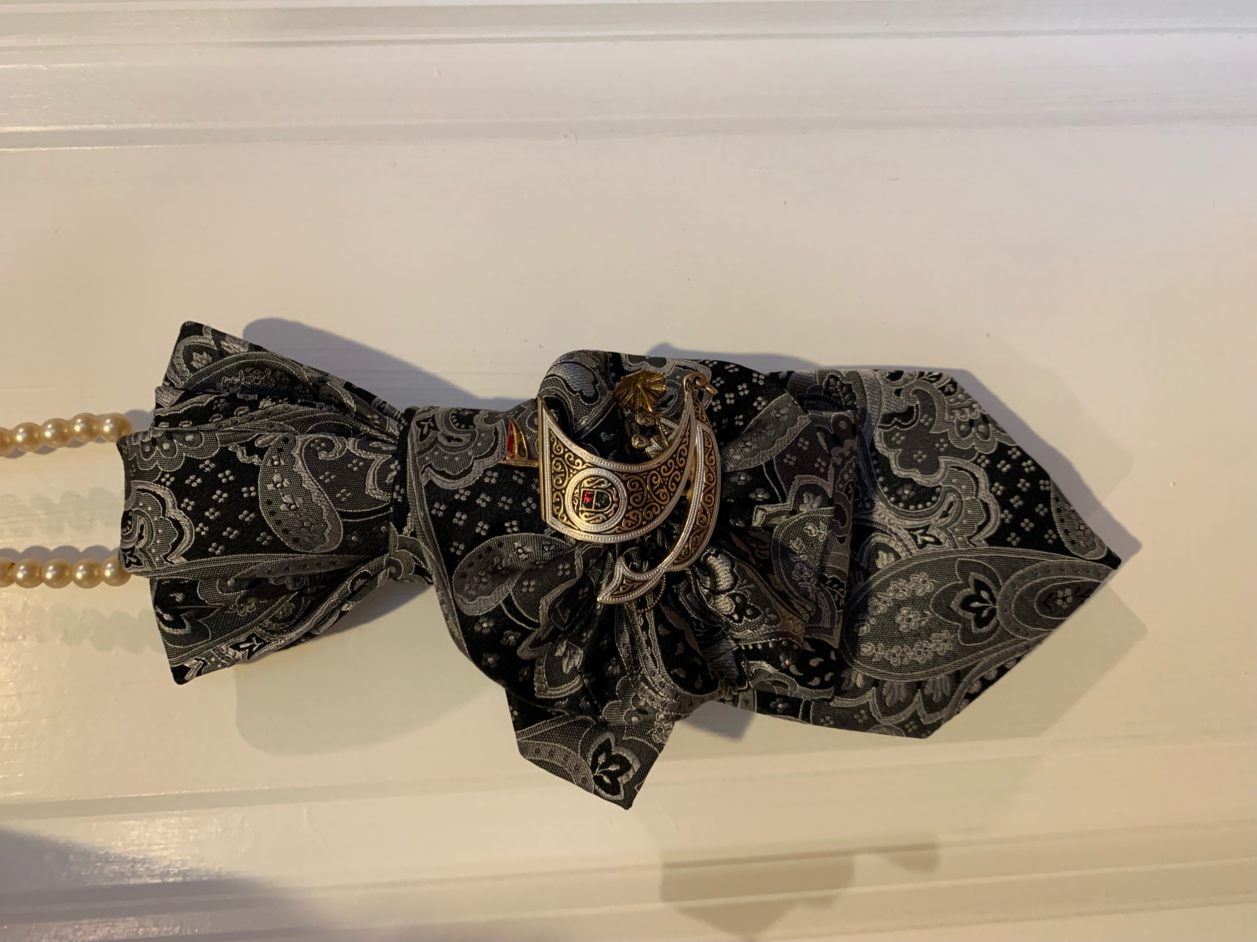 Black and white paisley patterned accessory with a gold crescent brooch, alongside reusable shopping bags repurposed from rice and feed sacks.