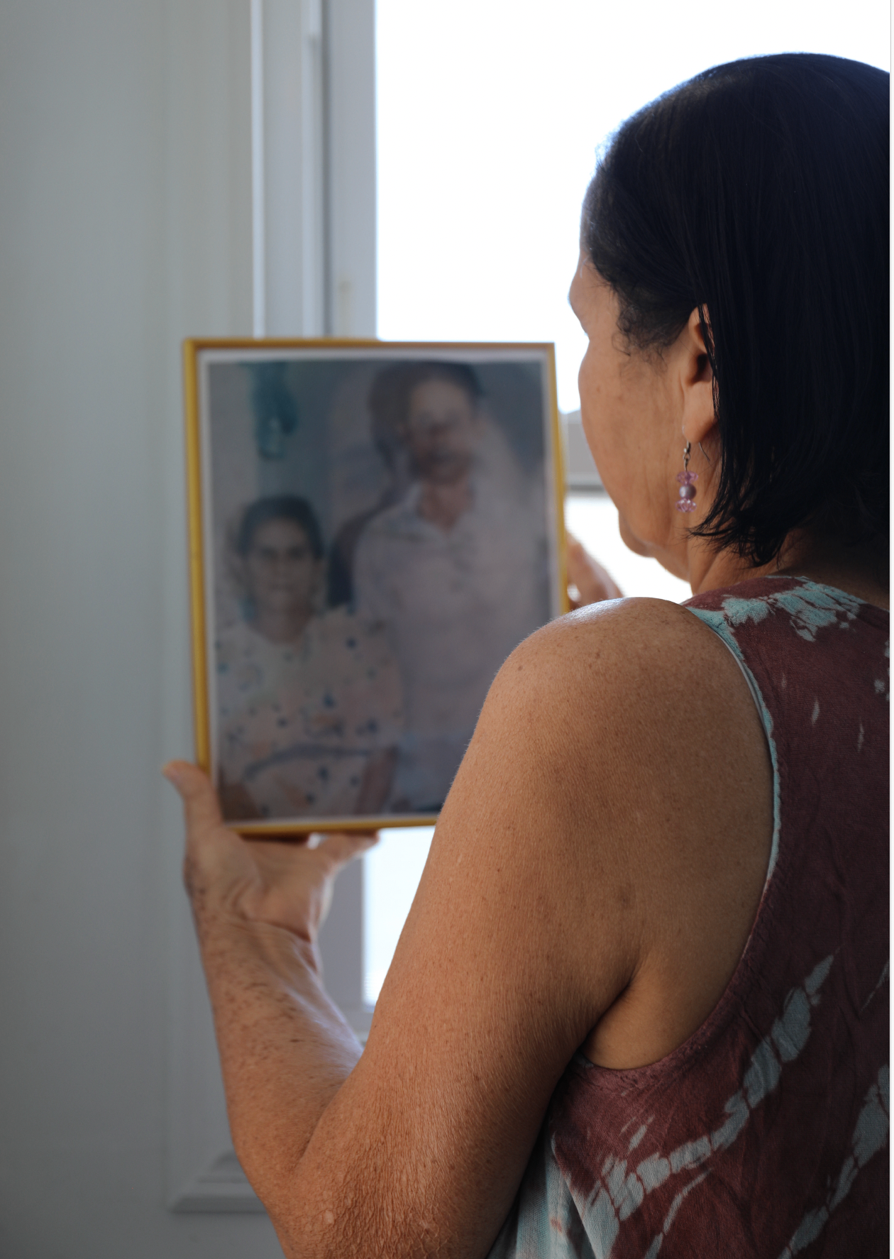 "Grandma & Great Grandparents" (2026), Canon EOS 5D Mark IV — a woman shot from behind, silhouetted against a bright window, holding up a framed vintage portrait of her grandparents.