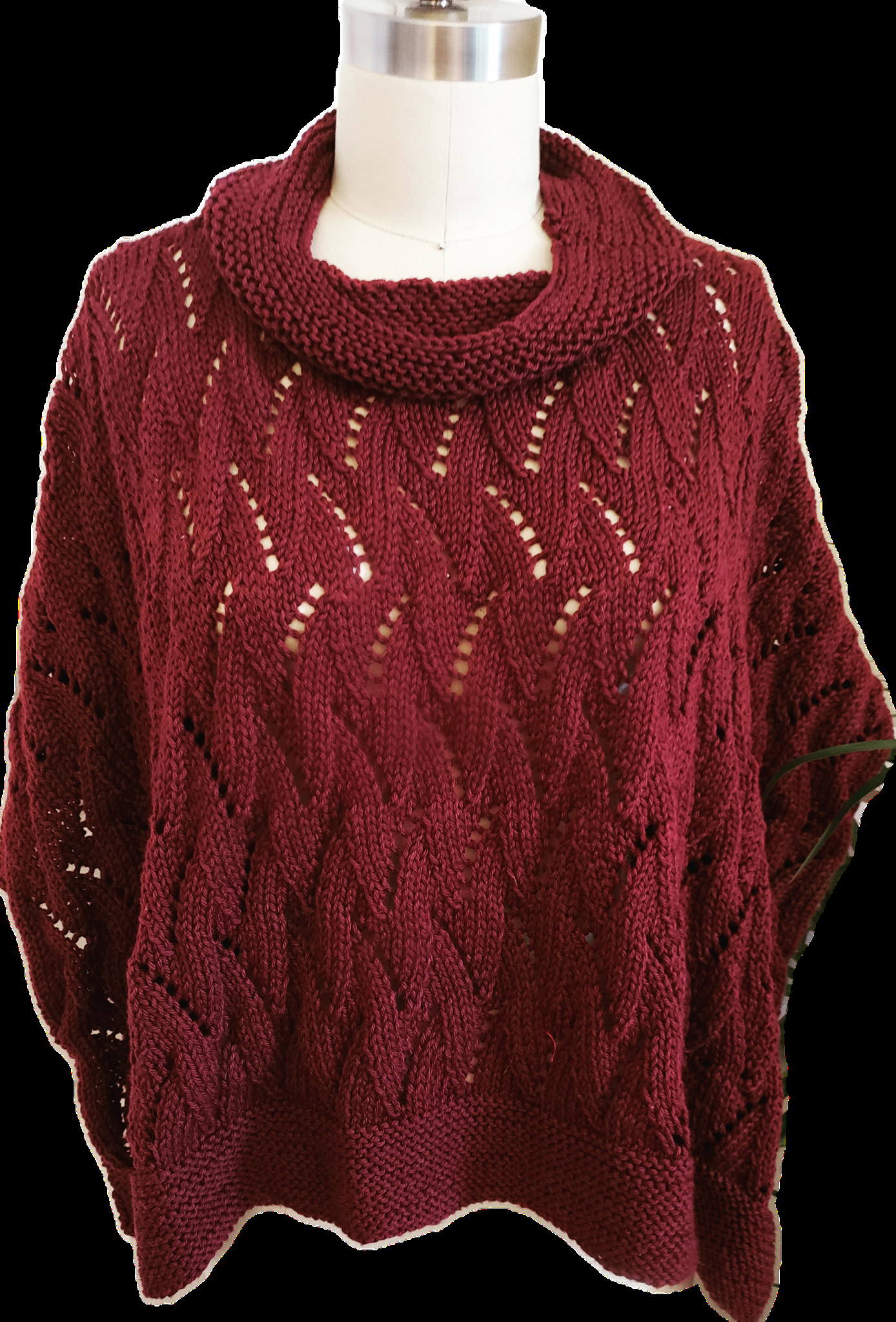 A maroon knitted poncho with cable and lace pattern displayed on a mannequin.