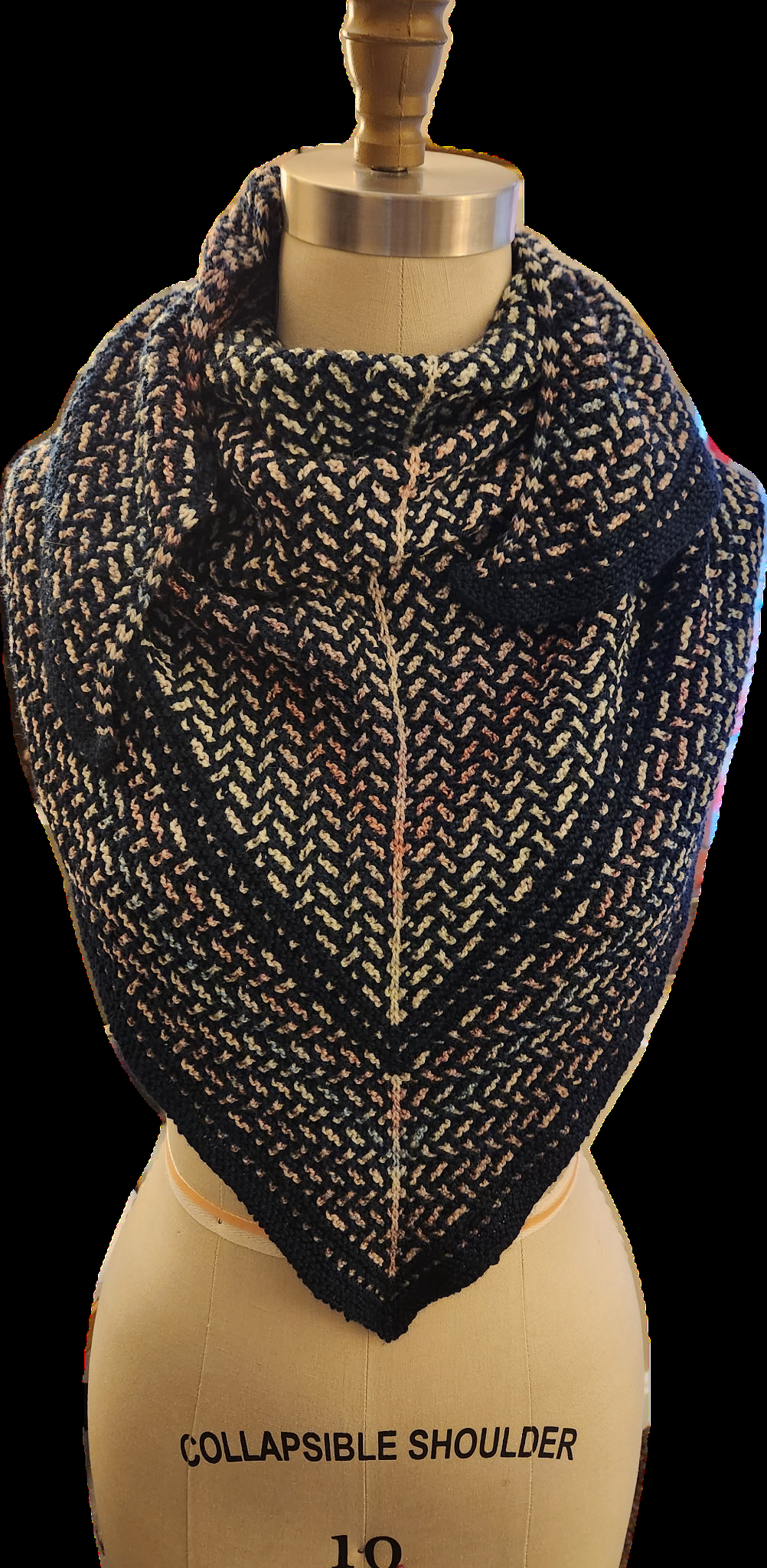 A dark, textured herringbone-patterned knitted cowl on a mannequin torso.